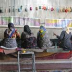 A row of women weaving at a loom