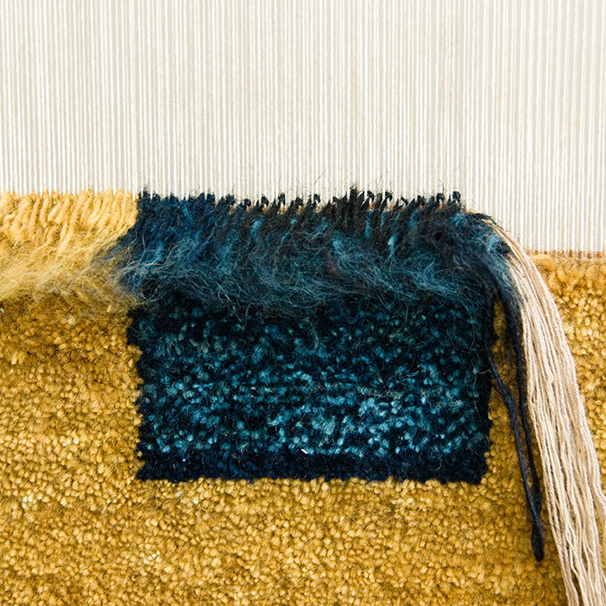 Blue and gold vegetable dyed Persian wool knotted onto the warp and weft of a fine handmade area rug in the making